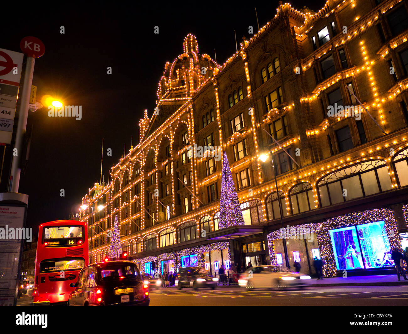 I grandi magazzini Harrods al tramonto con le luci di Natale shoppers e passaggio di taxi e autobus rossi Knightsbridge London SW1 Foto Stock