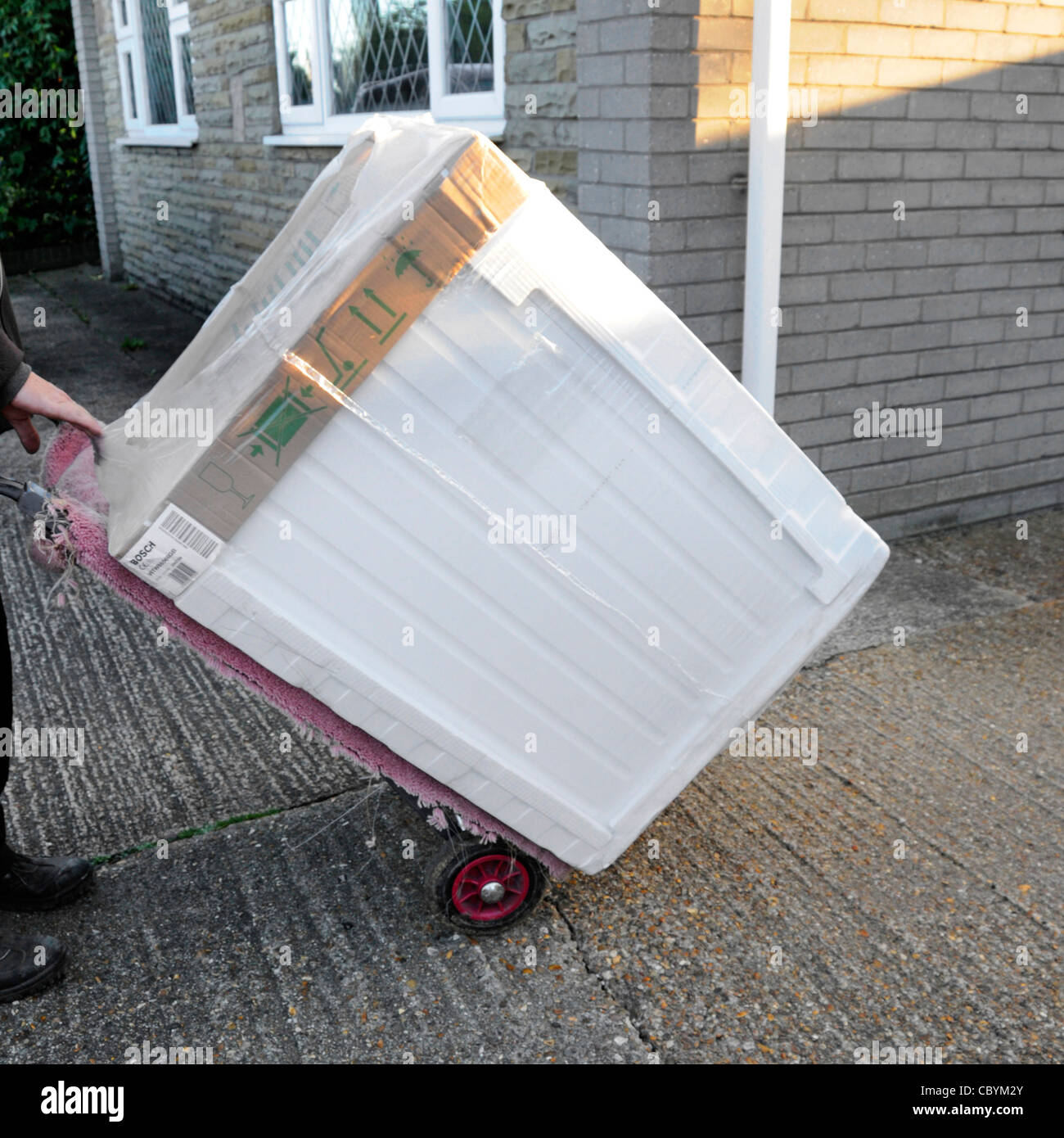Uomo di consegna mediante carrello di servizio in grado di consegnare un nuovo Bosch asciugatrice dall apparecchio elettrico merci bianco retail business di alimentazione ad una casa in Inghilterra Essex REGNO UNITO Foto Stock