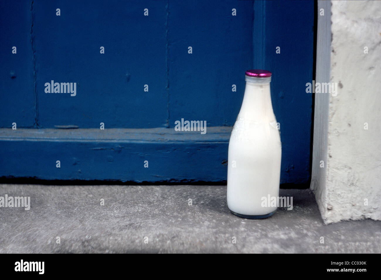 Una bottiglia di vetro del latte fresco è consegnato a domicilio di un cottage con una porta blu in Inghilterra del pittoresco Cotswolds area della Gran Bretagna (GB). Foto Stock