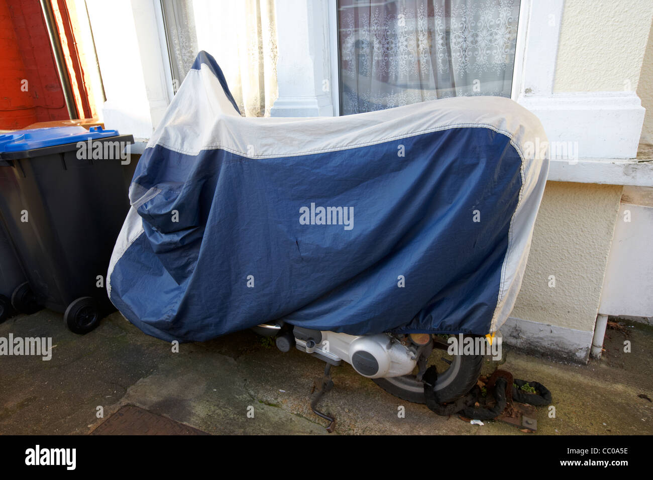 Moto scooter coperti con copertura protettiva e incatenato al suolo al di fuori di una casa nel nord di Londra Inghilterra REGNO UNITO Foto Stock