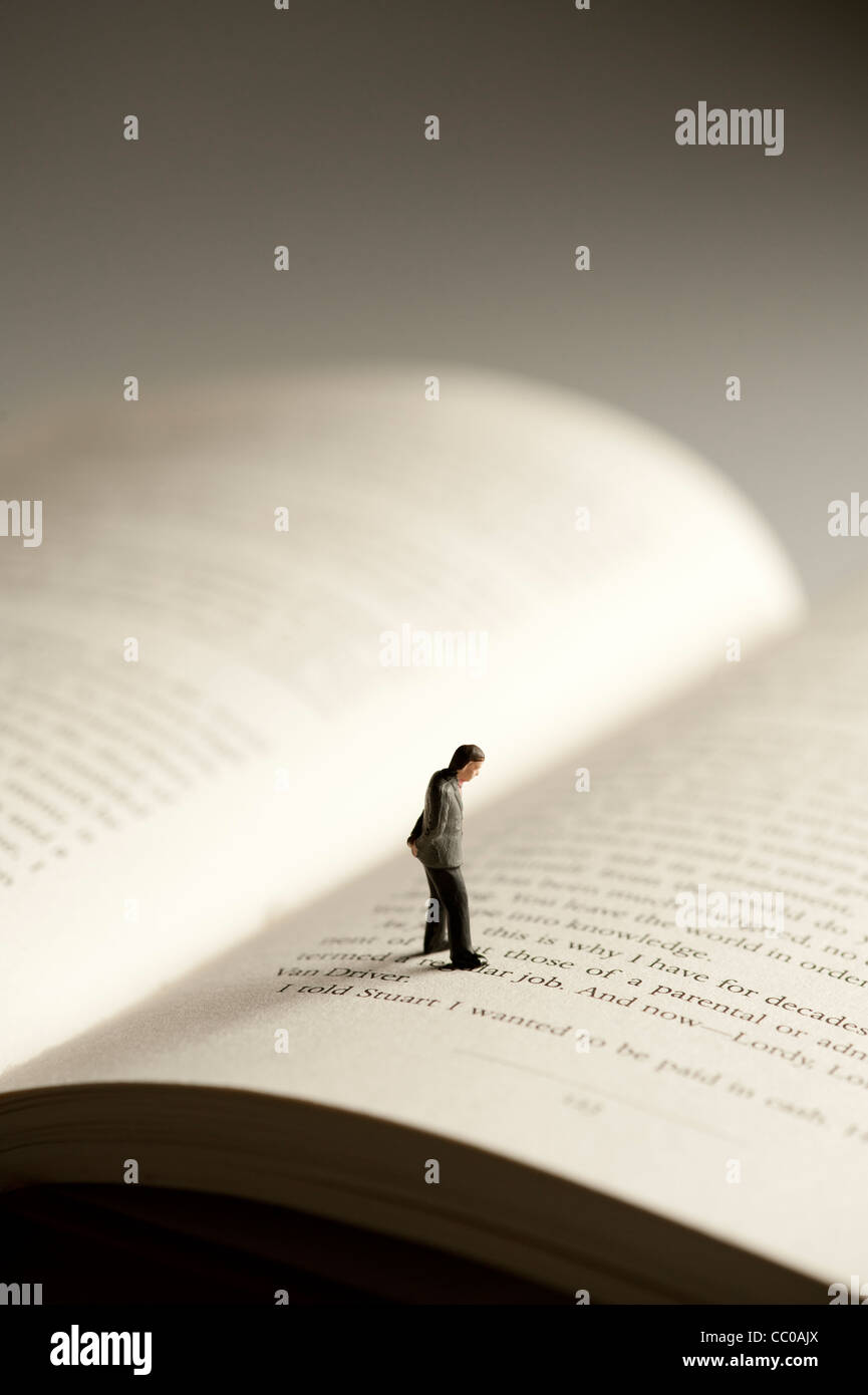 Una piccola figura di un uomo che cammina su un libro aperto - immagine concettuale per l alfabetizzazione e la lettura Foto Stock