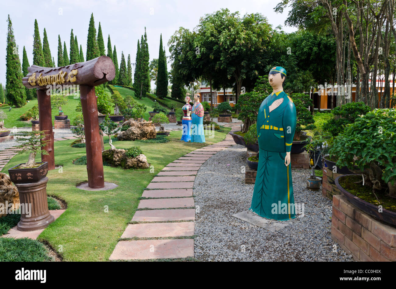 Le statue a grandezza naturale che assomigliano a tall matrioska bambole, arco in legno & percorso in corrispondenza di bonzai giardino interno all Expo nel nord della Thailandia Foto Stock