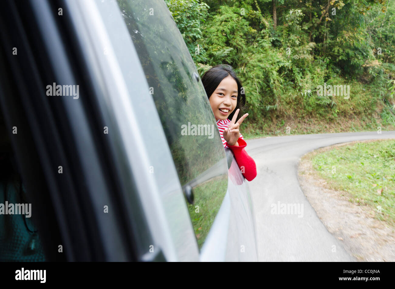 Carino di nove anni ragazza tailandese sorrisi e lampeggia V segno dal retro del pickup truck nel nord della Thailandia Foto Stock