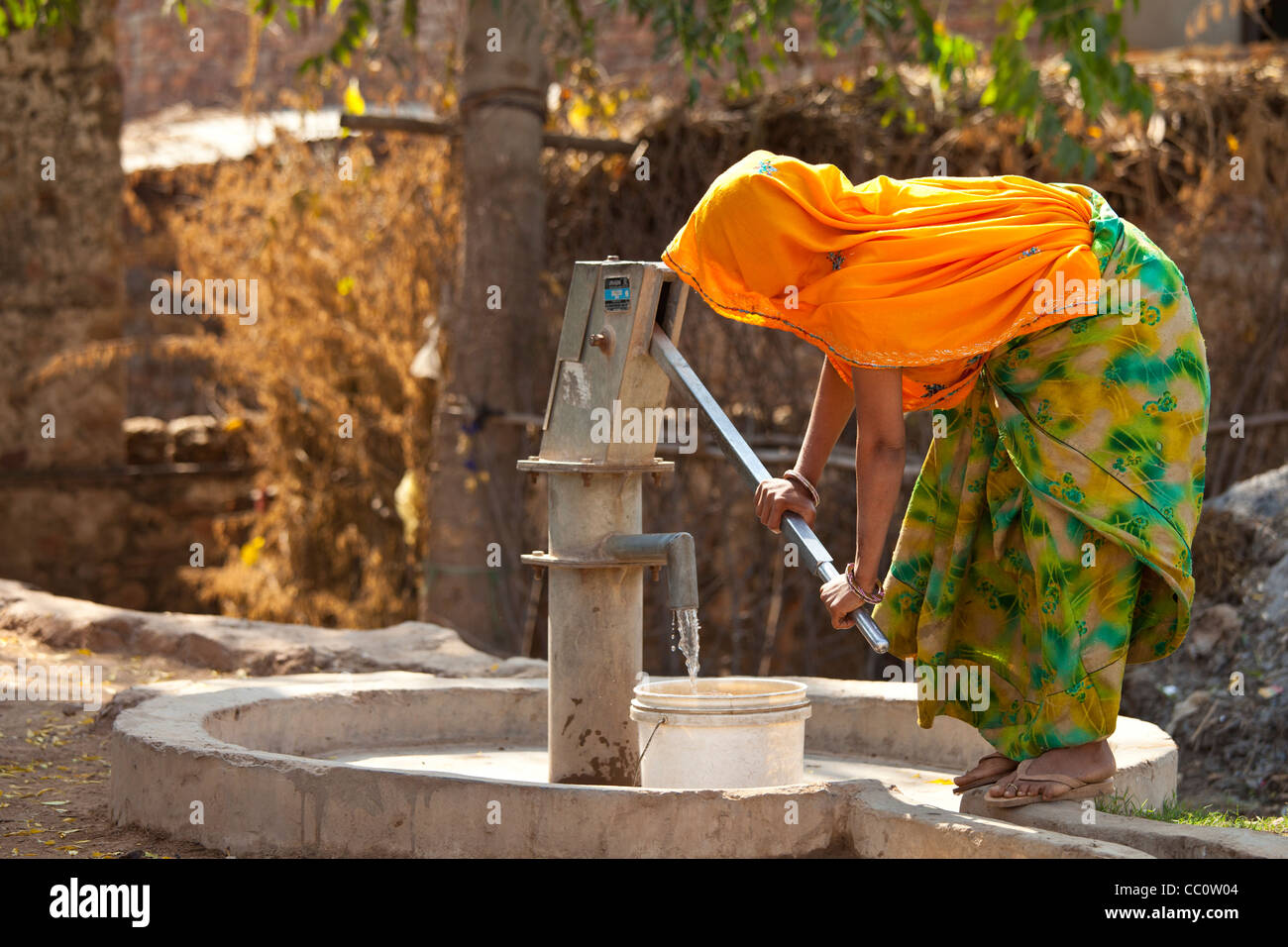 Donna indiana abitante il pompaggio di acqua da un pozzo a Sawai Madhopur nel Rajasthan, India settentrionale Foto Stock