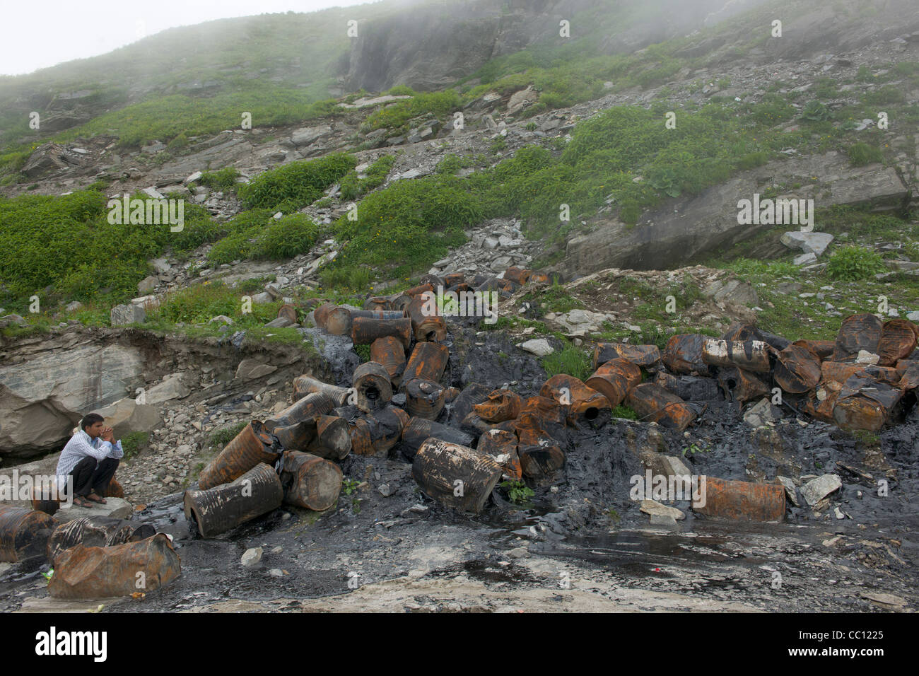 L'uomo squatting da bruciato i fusti di carburante al Rohtang Pass, sull'autostrada Leh-Manali, Himachal Pradesh, India Foto Stock