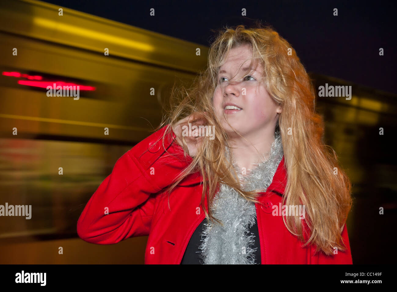 Teen ragazza con treno notte accelerando dietro di lei e soffiare i suoi lunghi capelli biondi Foto Stock