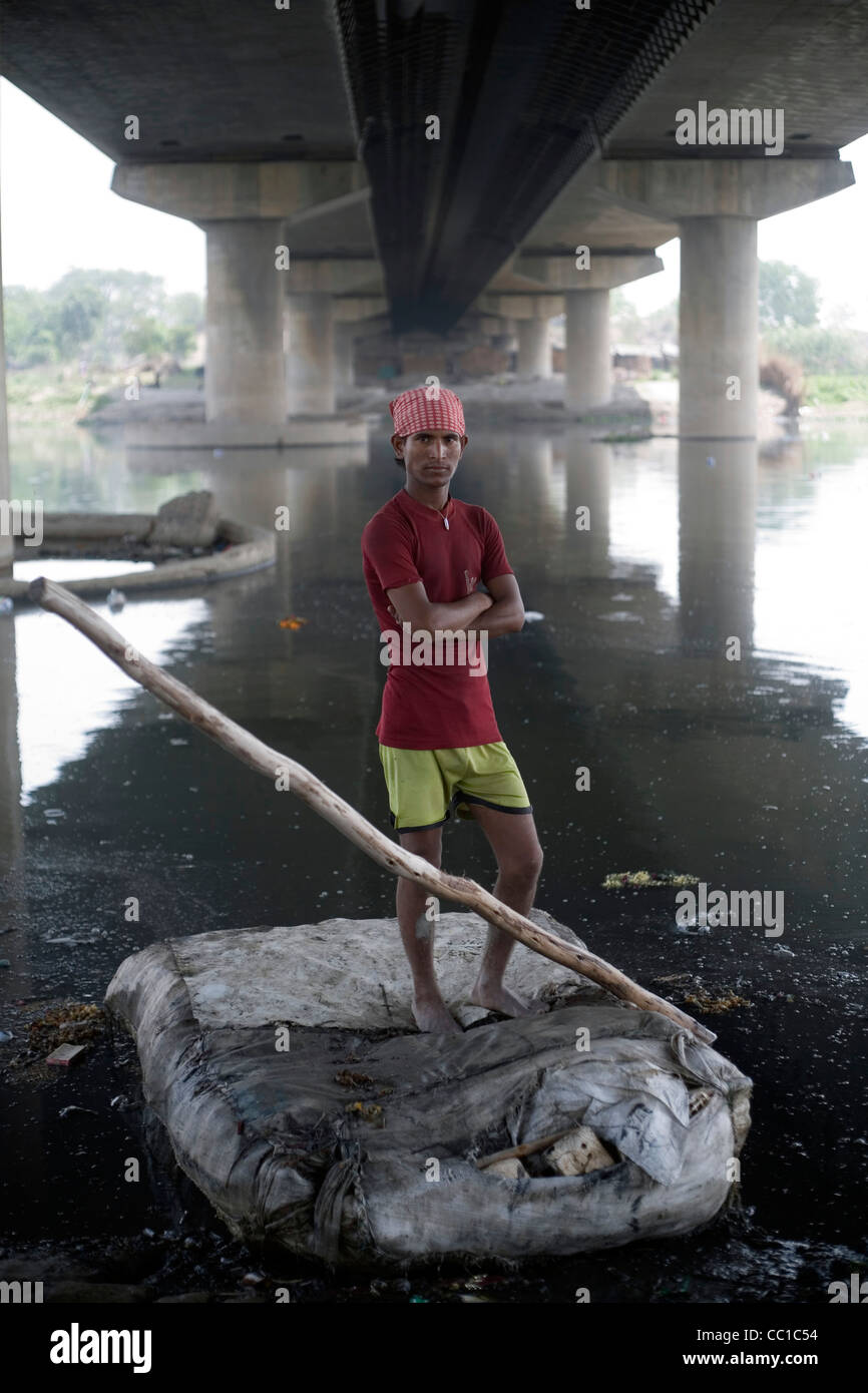 Un giovane che scavenger di reti a strascico per recuperare su una zattera, al di sotto del ponte stradale attraverso il fiume Yamuna, Nuova Delhi. Foto Stock