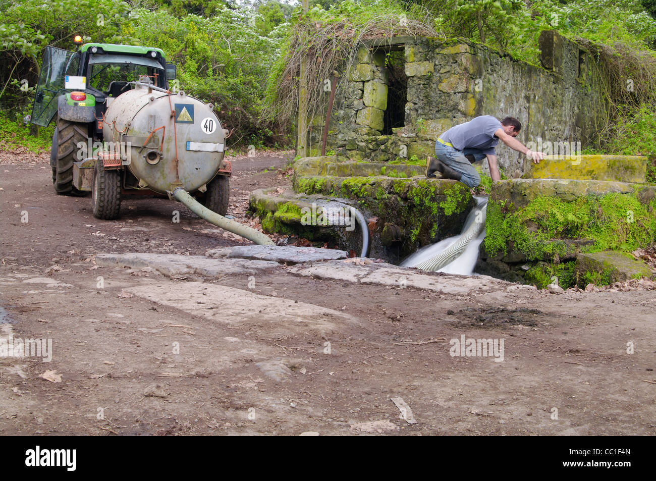 Agricoltore che porta acqua al bestiame dal flusso d'acqua naturale. Agricoltore nelle Azzorre che raccoglie l'acqua da una struttura in pietra utilizzando un'autocisterna per trattori a tr Foto Stock