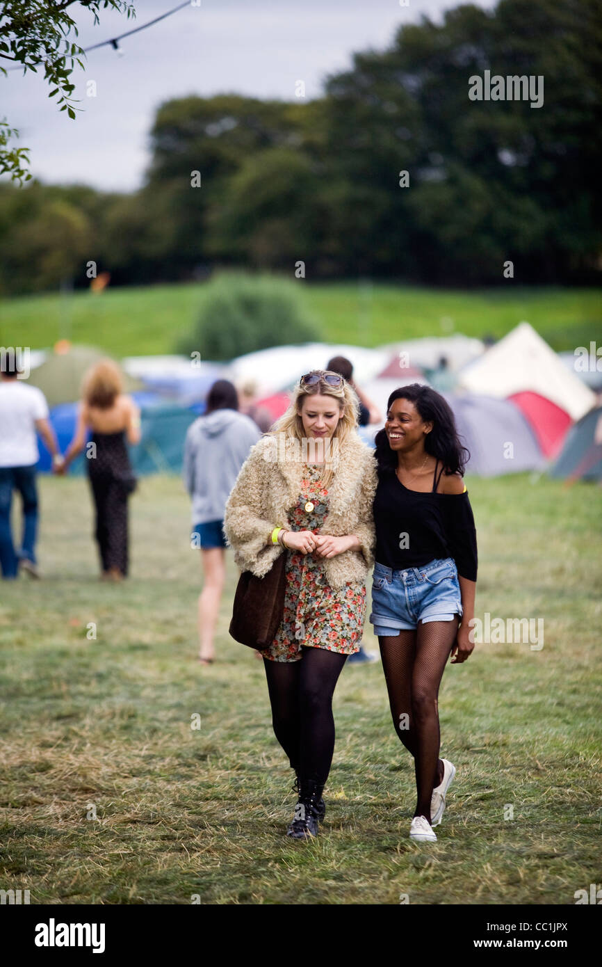 Due amiche a piedi attraverso un campo a Standon Calling Festival nel Hertfordshire, Regno Unito Foto Stock