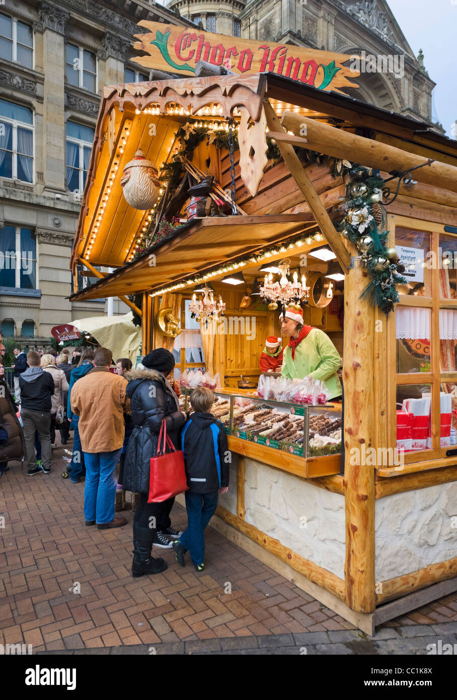 La famiglia di fronte a una bancarella vendendo cioccolata al Tedesco Francoforte Mercatino di Natale, Victoria Square, Birmingham, Regno Unito Foto Stock