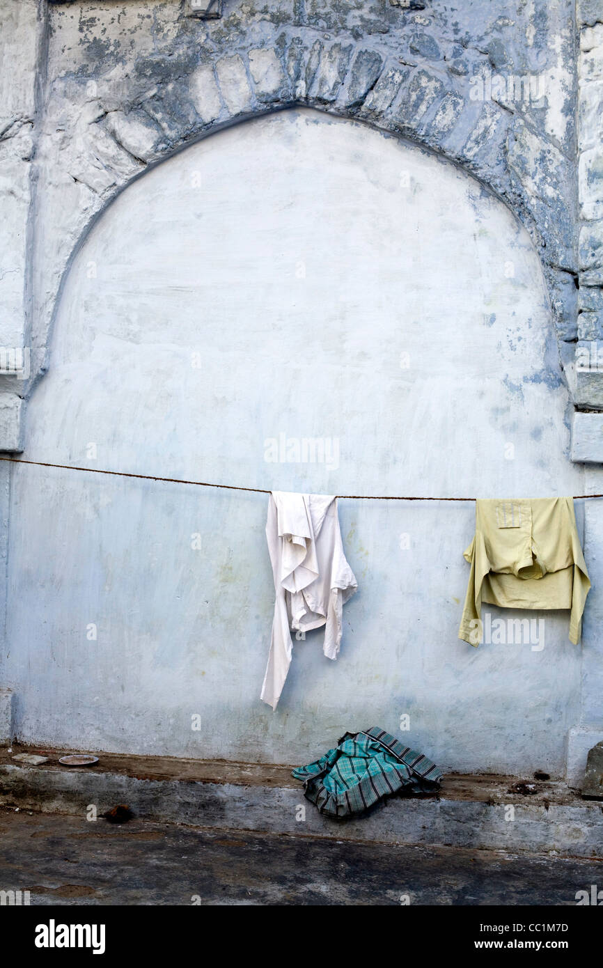 Due magliette appendere su una linea di lavaggio da una parete blu su una strada a Delhi, India Foto Stock