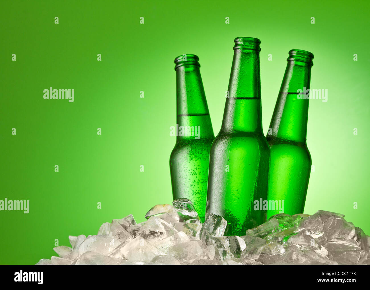 Tre bottiglie di birra sempre fresco in cubetti di ghiaccio. Isolato su una verde. Foto Stock