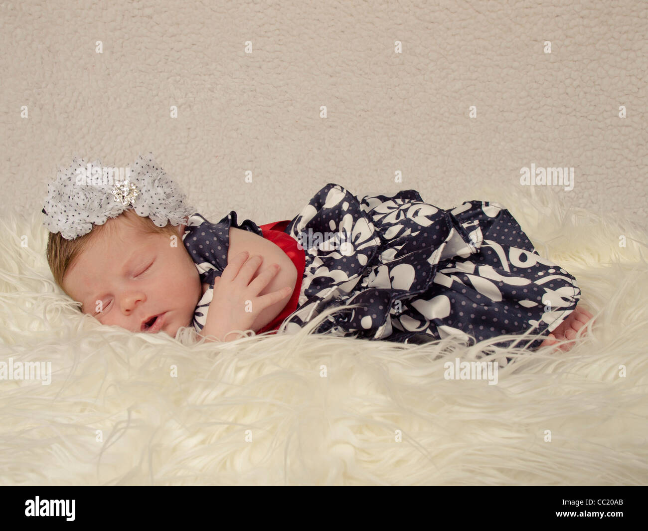 Ragazza neonata 9 giorni dormendo pacificamente su una pelliccia bianca coperta in un bel vestito e con archetto Foto Stock