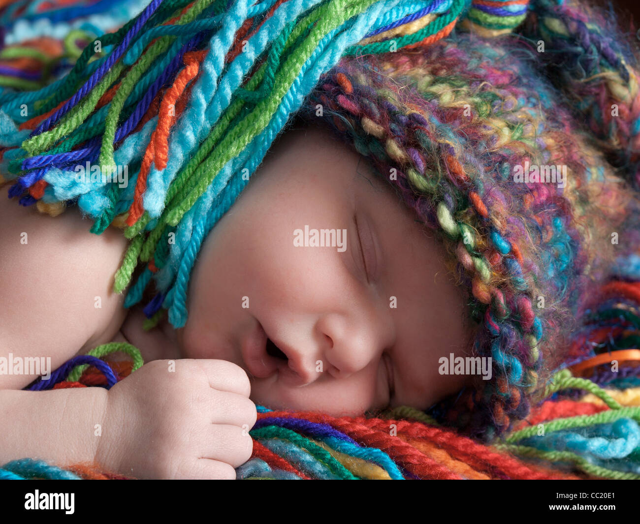 Neonato bambino addormentato serenamente nel suo berretto in maglia e corrispondenza di letto di filati multicolori. Foto Stock