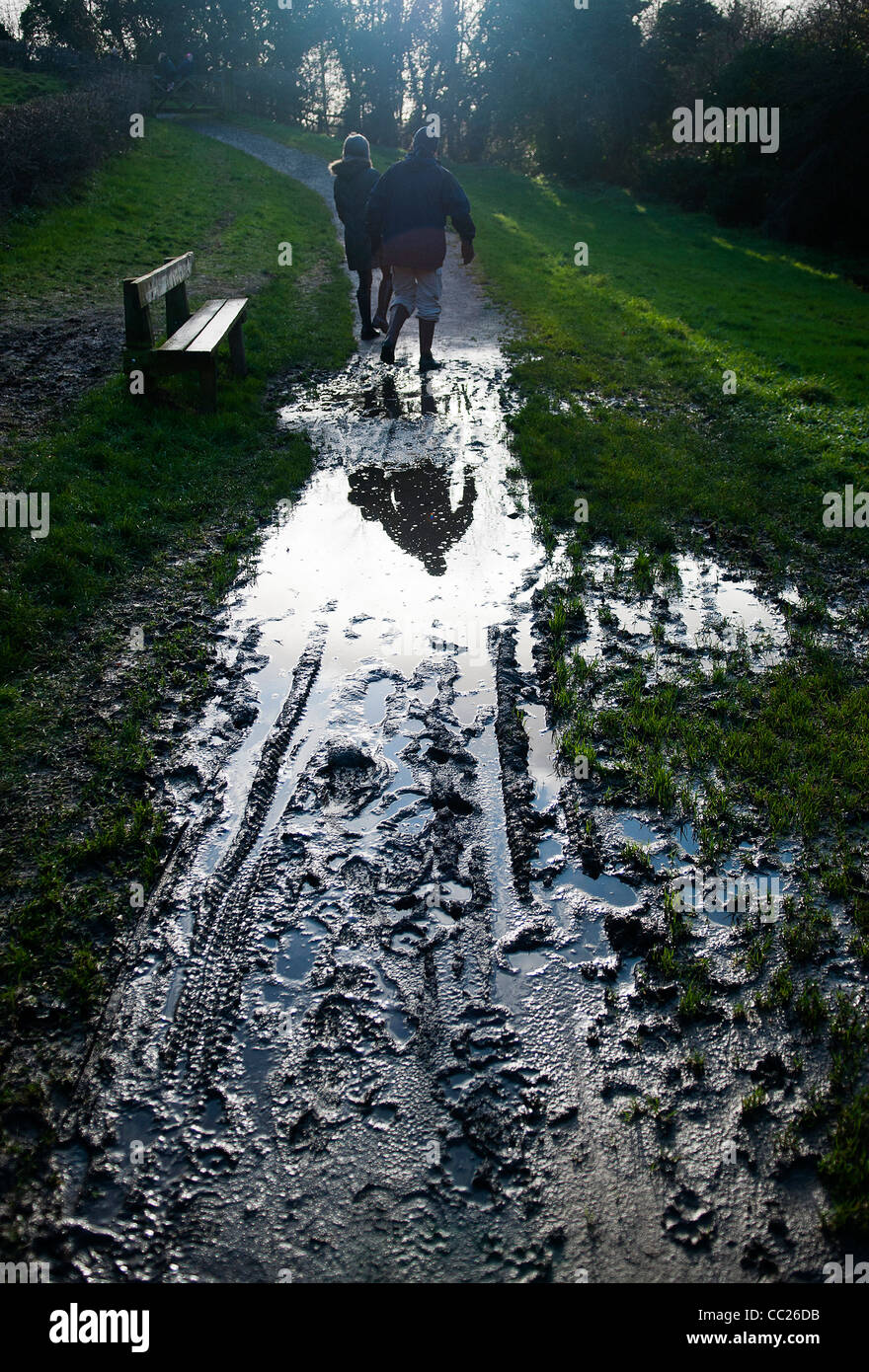 Giovane camminando con cautela sul sentiero fangoso, che si riflette in una pozzanghera, contro la luce Foto Stock