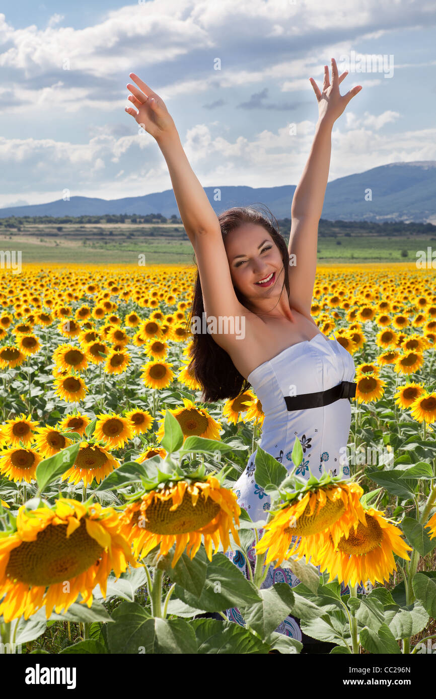 Felice giovane donna alzando le mani in un campo di girasoli Foto Stock