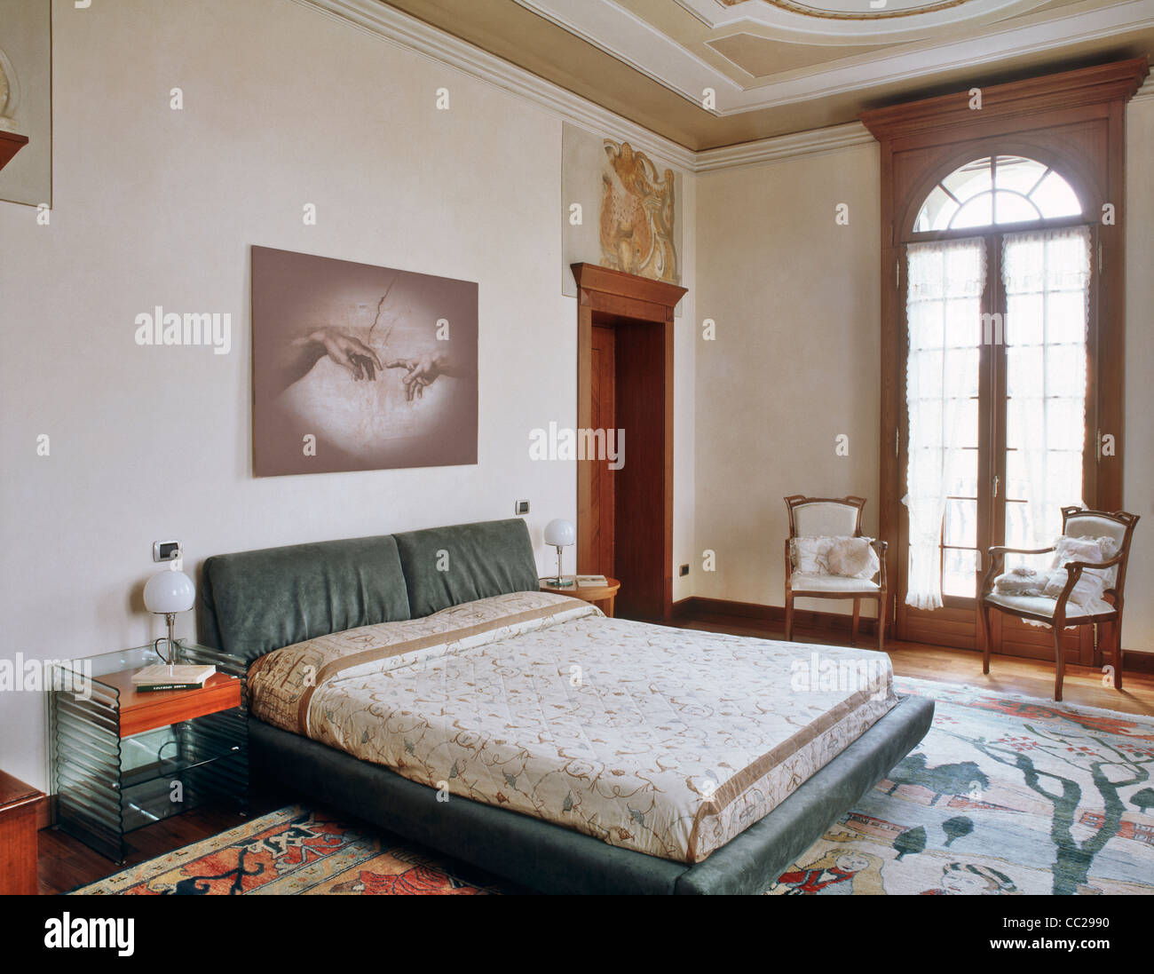 Grande camera da letto con affreschi e decorazioni, antico tappeto sul pavimento in legno e due piccoli poltroncina in legno vicino alla finestra Foto Stock