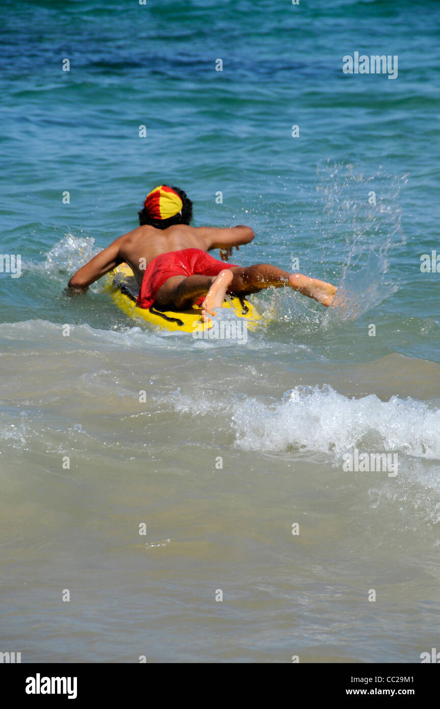 Un giovane bagnino entra in azione con la sua tavola da surf per salvare un nuotatore alla spiaggia di Bondi Foto Stock