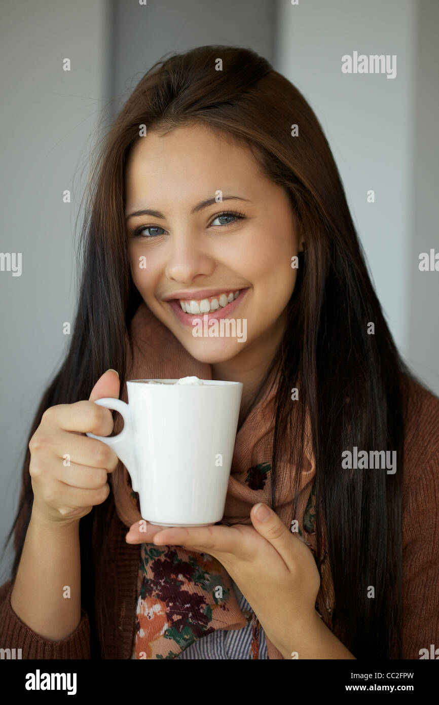 Giovane e bella ragazza con cioccolata calda e sorridente nella parte anteriore della fotocamera Foto Stock