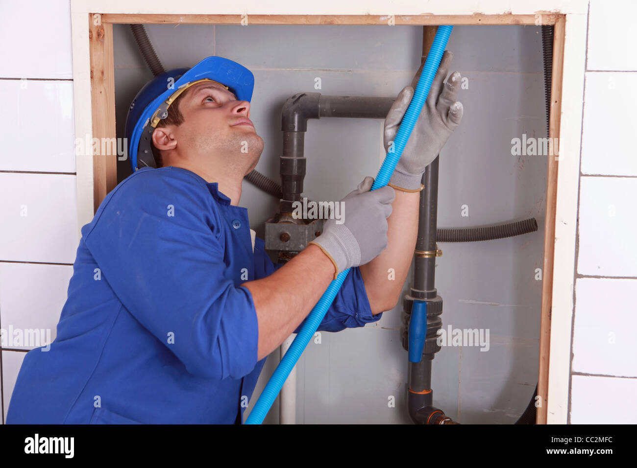 Plumber blu alimentazione tubo flessibile dietro una parete piastrellata Foto Stock