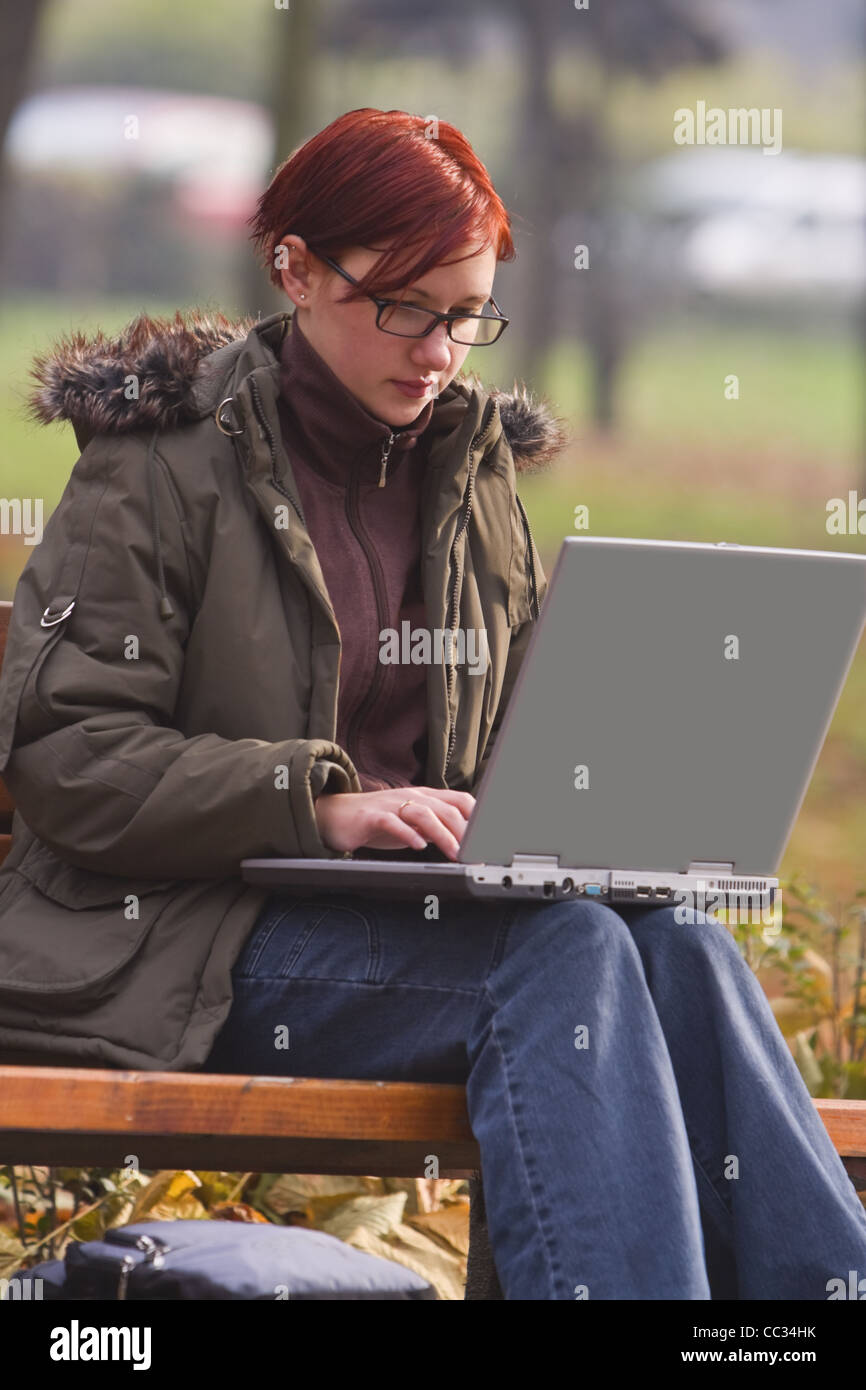 Redheaded ragazza che lavora su un computer portatile in un parco d'autunno. Foto Stock