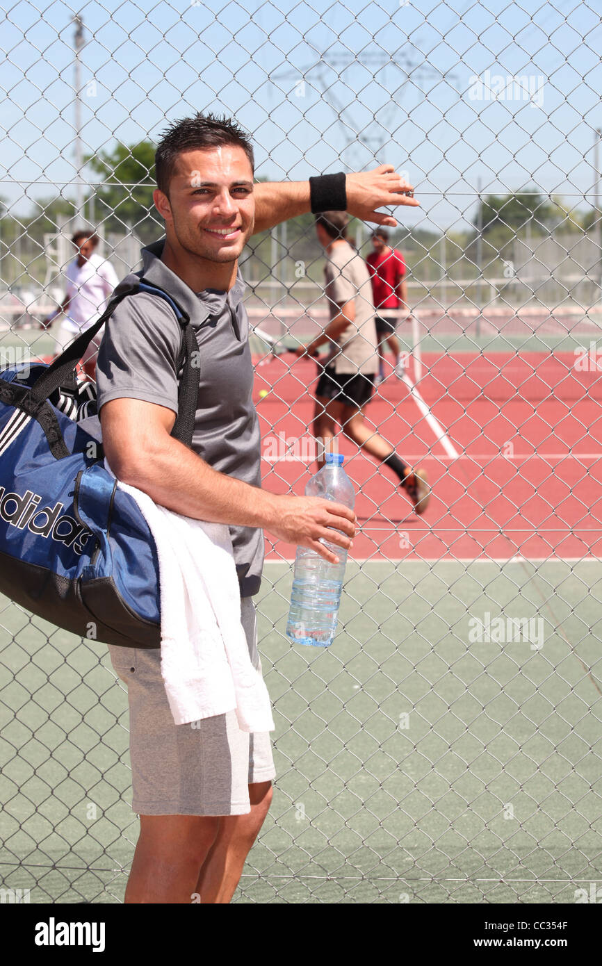 Uomo con borsa kit e una bottiglia di acqua la visione di gioco di tennis attraverso la recinzione di filo Foto Stock