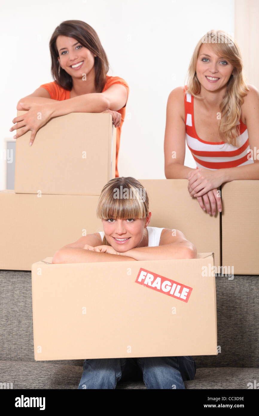 Tre giovani donne che pongono in una stanza piena di pacchetti scompattati Foto Stock