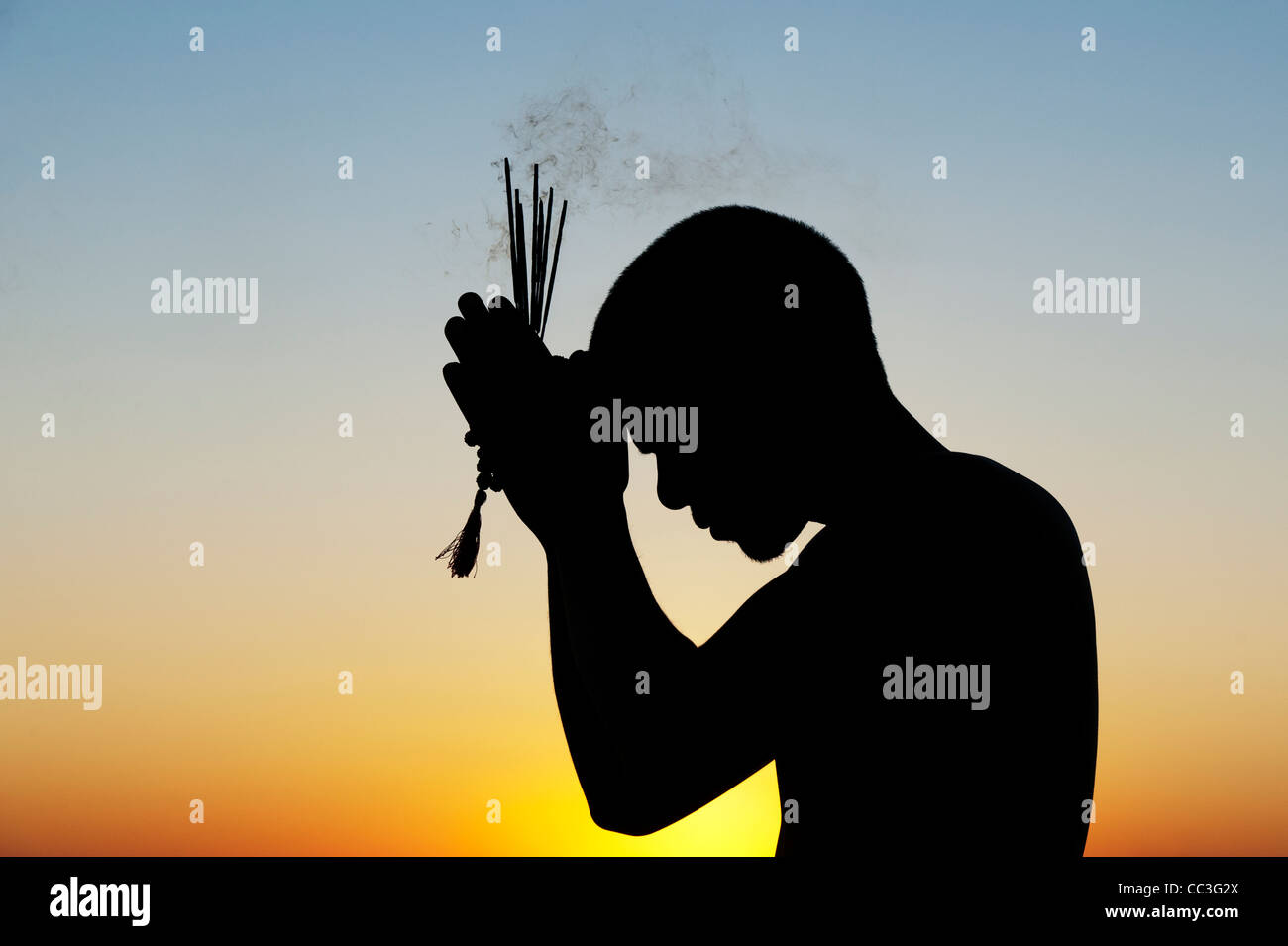 Pregando uomo indiano con bastoncini di incenso al tramonto. Silhouette. India Foto Stock