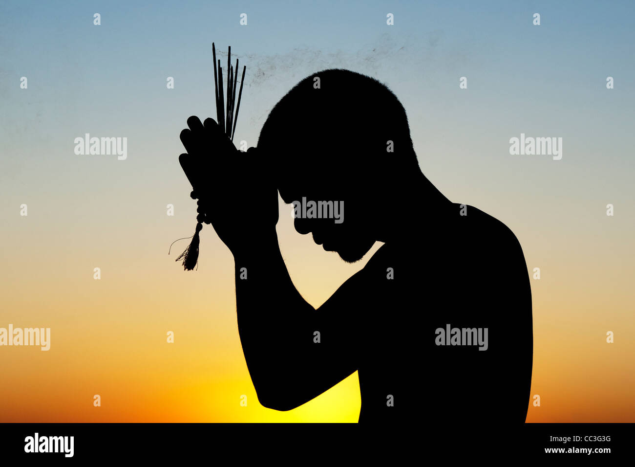 Pregando uomo indiano con bastoncini di incenso al tramonto. Silhouette. India Foto Stock