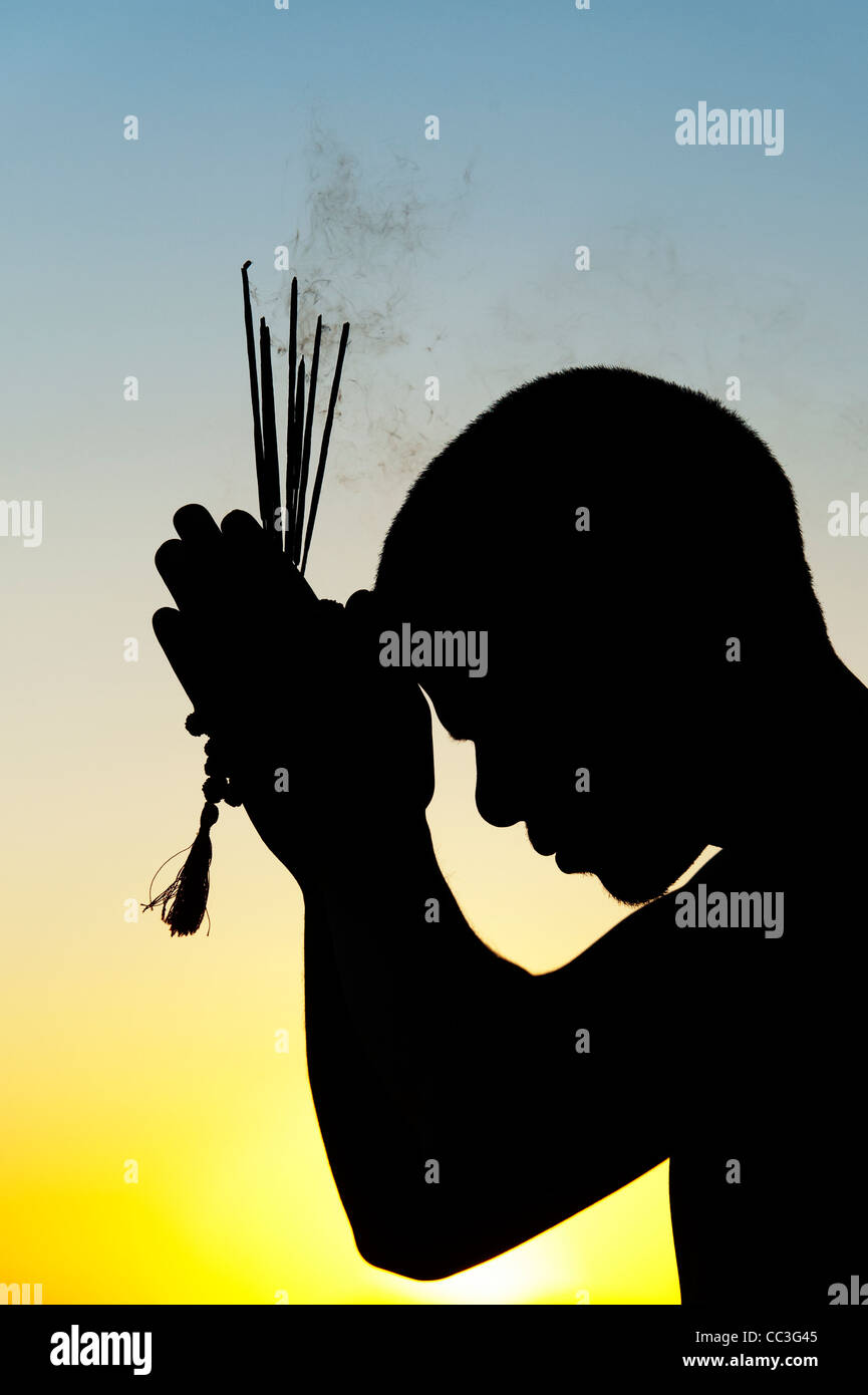 Pregando uomo indiano con bastoncini di incenso al tramonto. Silhouette. India Foto Stock