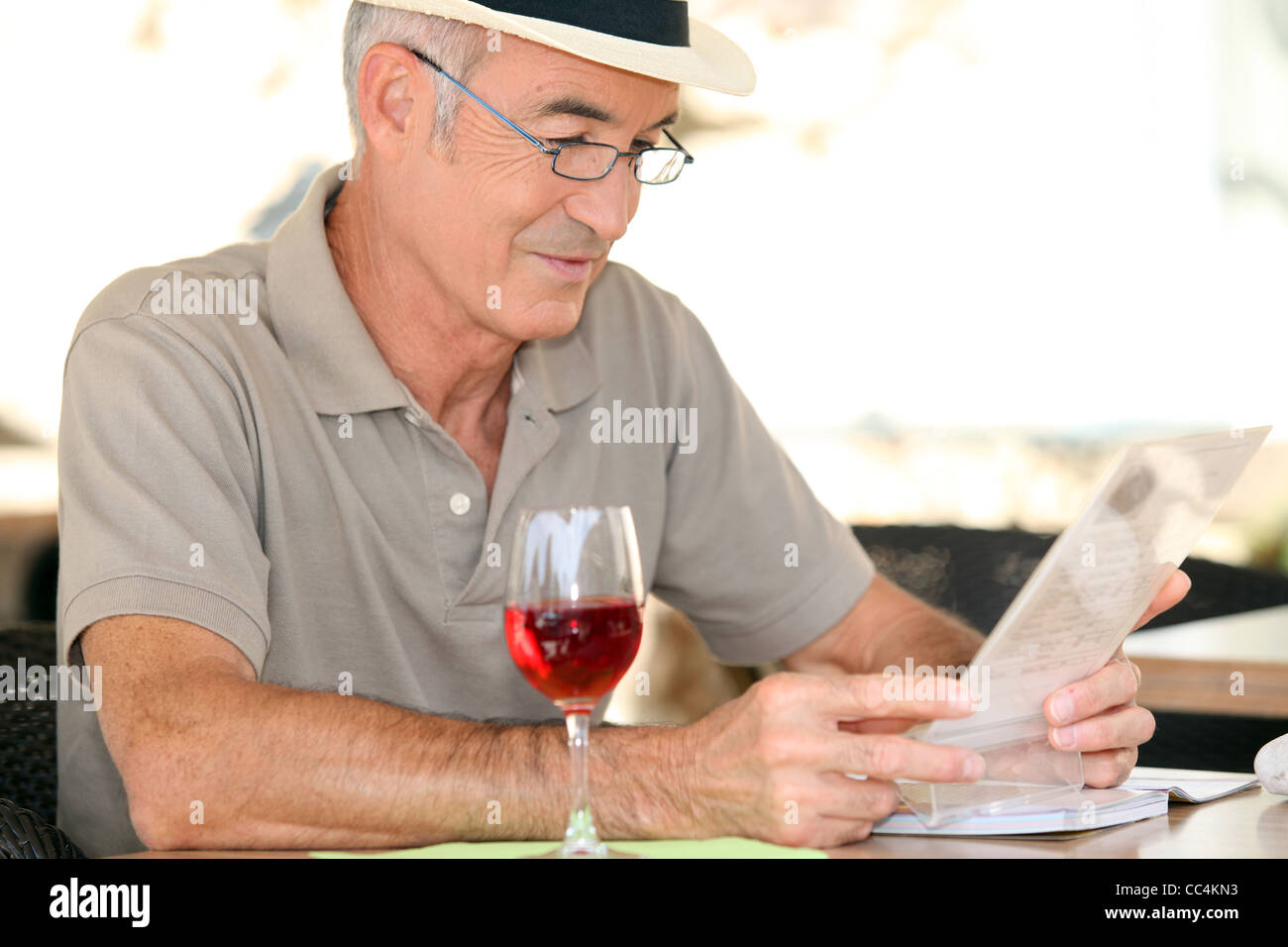 Anziano gentiluomo seduto nella caffetteria di bere un bicchiere di vino rosso Foto Stock