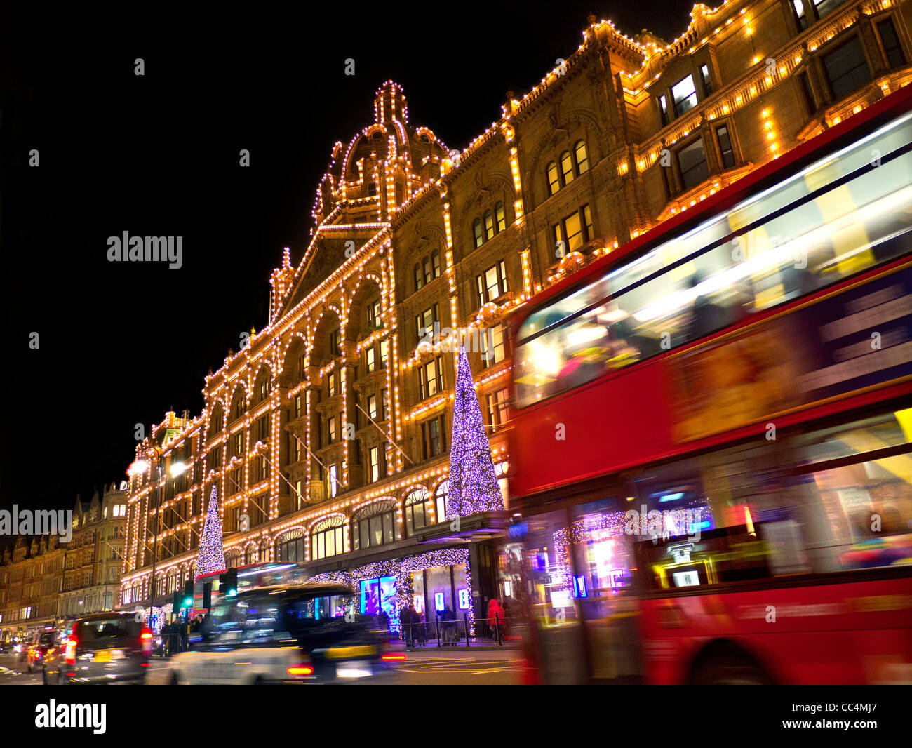 I grandi magazzini Harrods al tramonto con le luci di Natale shoppers e passaggio di taxi e autobus rossi Knightsbridge London SW1 Foto Stock