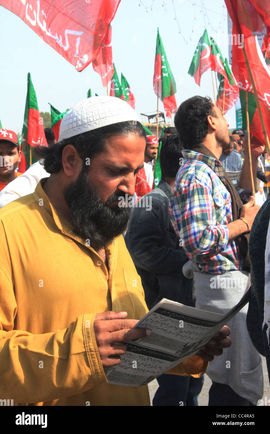 Un uomo legge letteratura di partito come egli attende in fila per entrare in un rally detenute dal Pakistan Tehreek-E-Insaf a Karachi in Pakistan Foto Stock