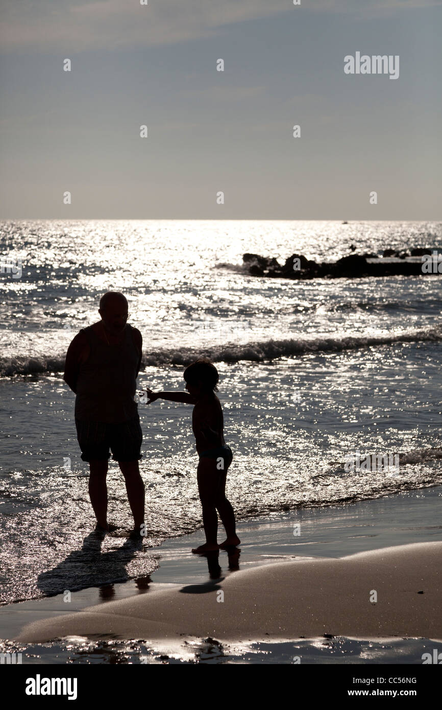 Nonno e nipote stagliano contro il riflesso del sole via mare a Anzio beach Foto Stock