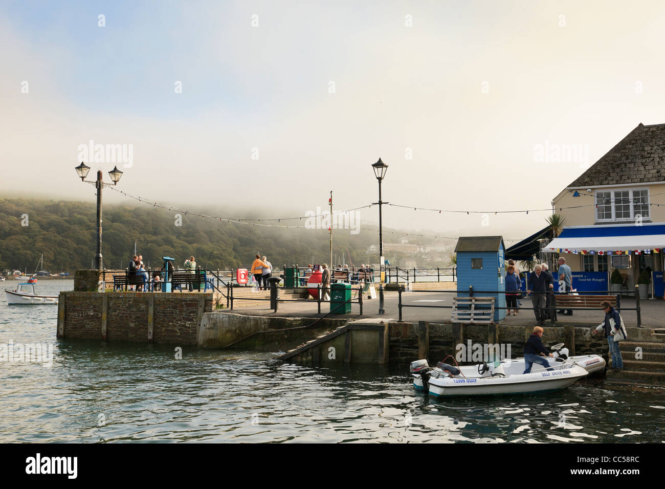 Fowey, Cornwall, Inghilterra, Regno Unito, Gran Bretagna. Persone in Riverside Quay con la foschia marina clearing sulle colline Foto Stock
