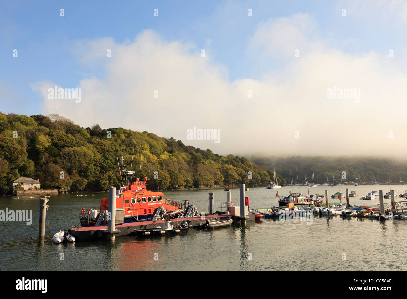 Fowey Cornwall Inghilterra UK Gran Bretagna scialuppa di salvataggio e barche ormeggiate dal molo sul Fiume Fowey con nebbia di mare clearing sulle colline Foto Stock