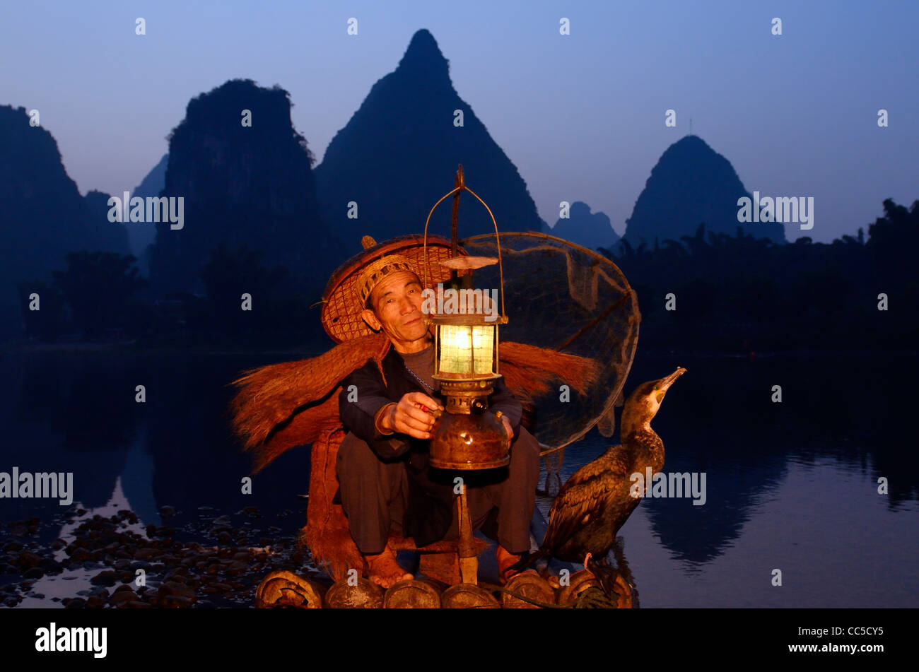 Cormorano pescatore lanterna di illuminazione con bird su zattera di bambù all'alba con silhouette di vette carsiche sulla riva del fiume Li Yangshuo Cina Foto Stock