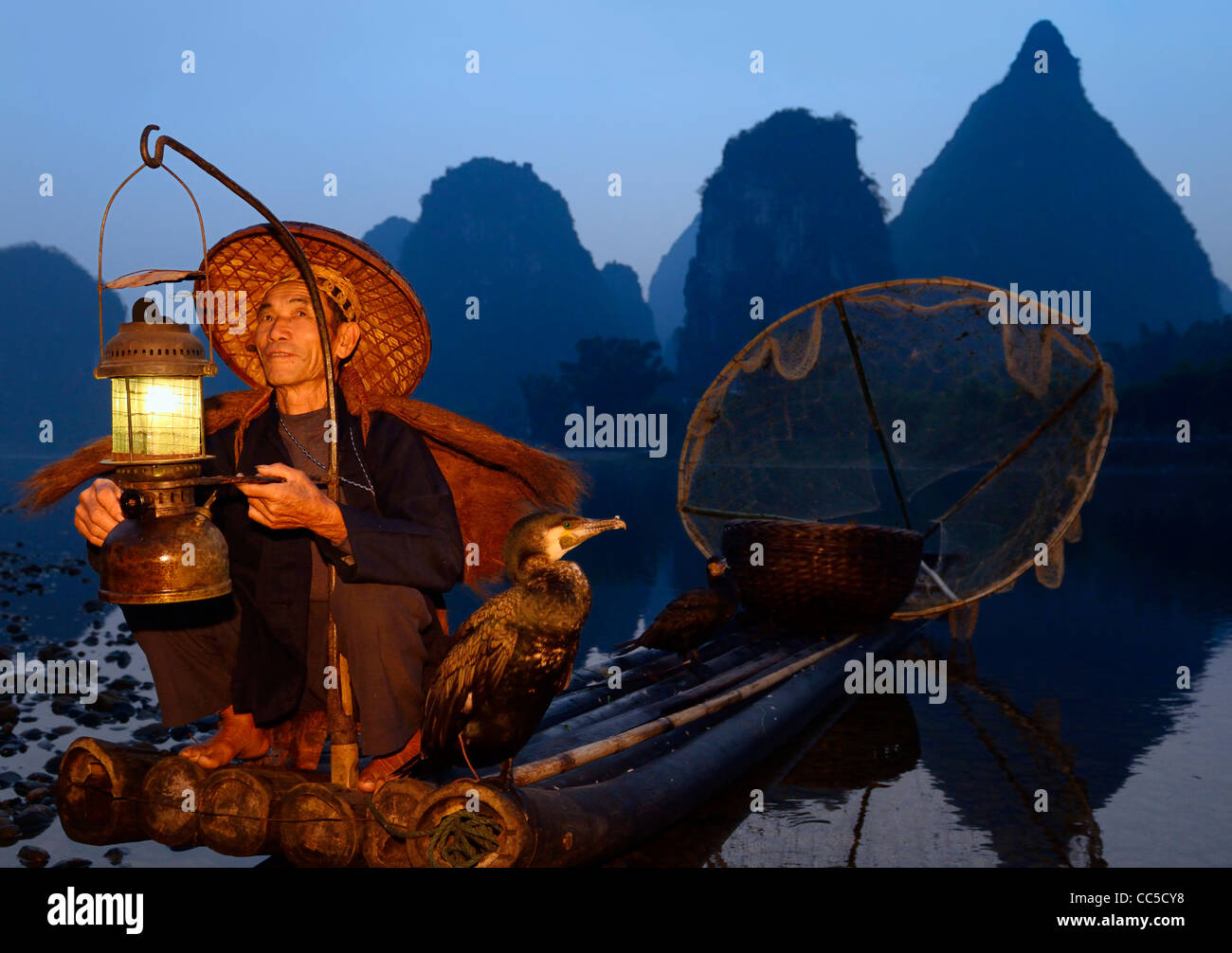 Pescatore con la lanterna su una zattera di bamboo con cormorani all'alba con ambiente carsico picchi sulla riva del fiume Li Yangshuo Cina Foto Stock