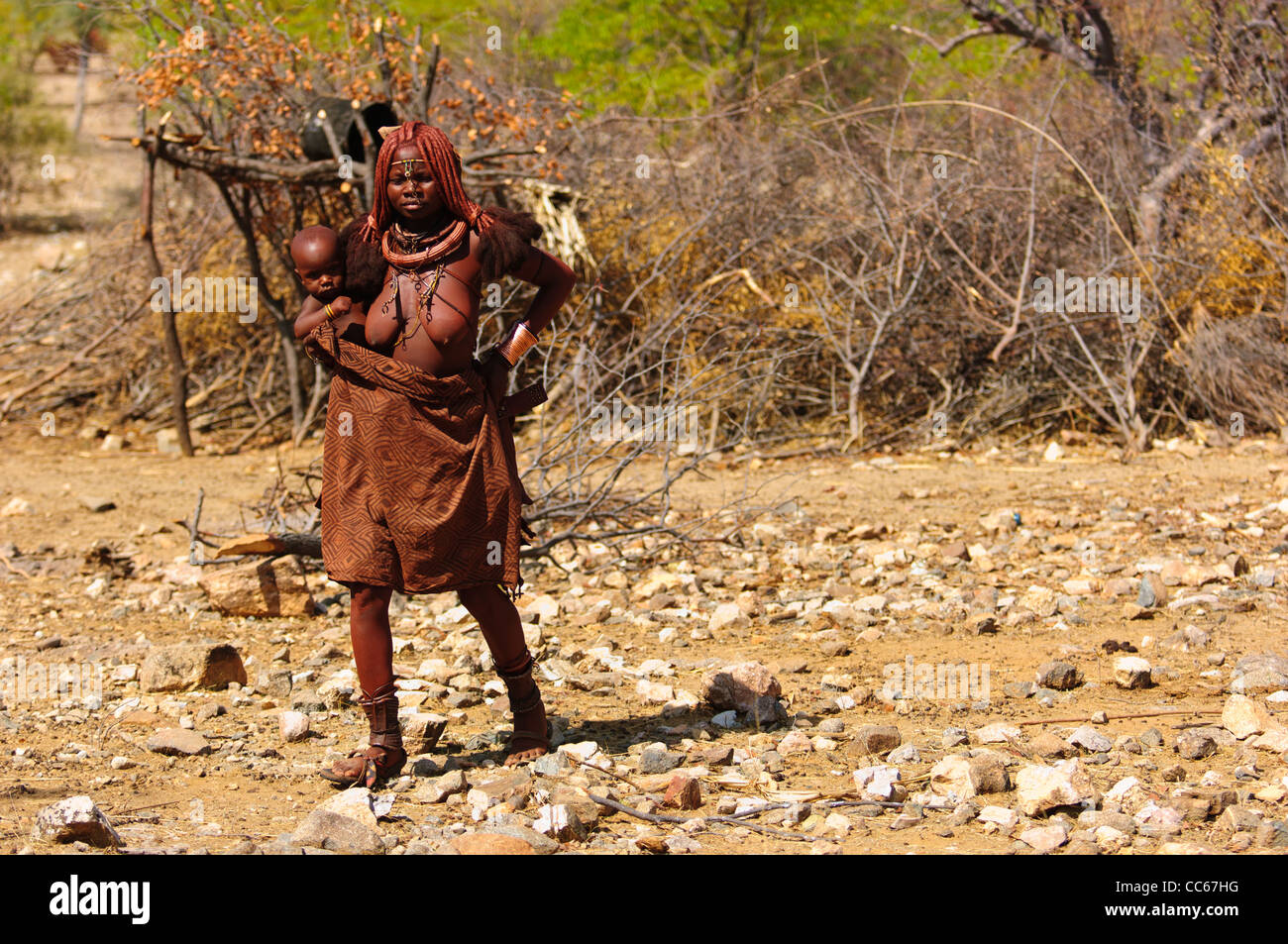 Himba la madre e il bambino di fronte alla centrale di enclosure di bestiame del loro villaggio. Kaokoland, Namibia settentrionale. Foto Stock