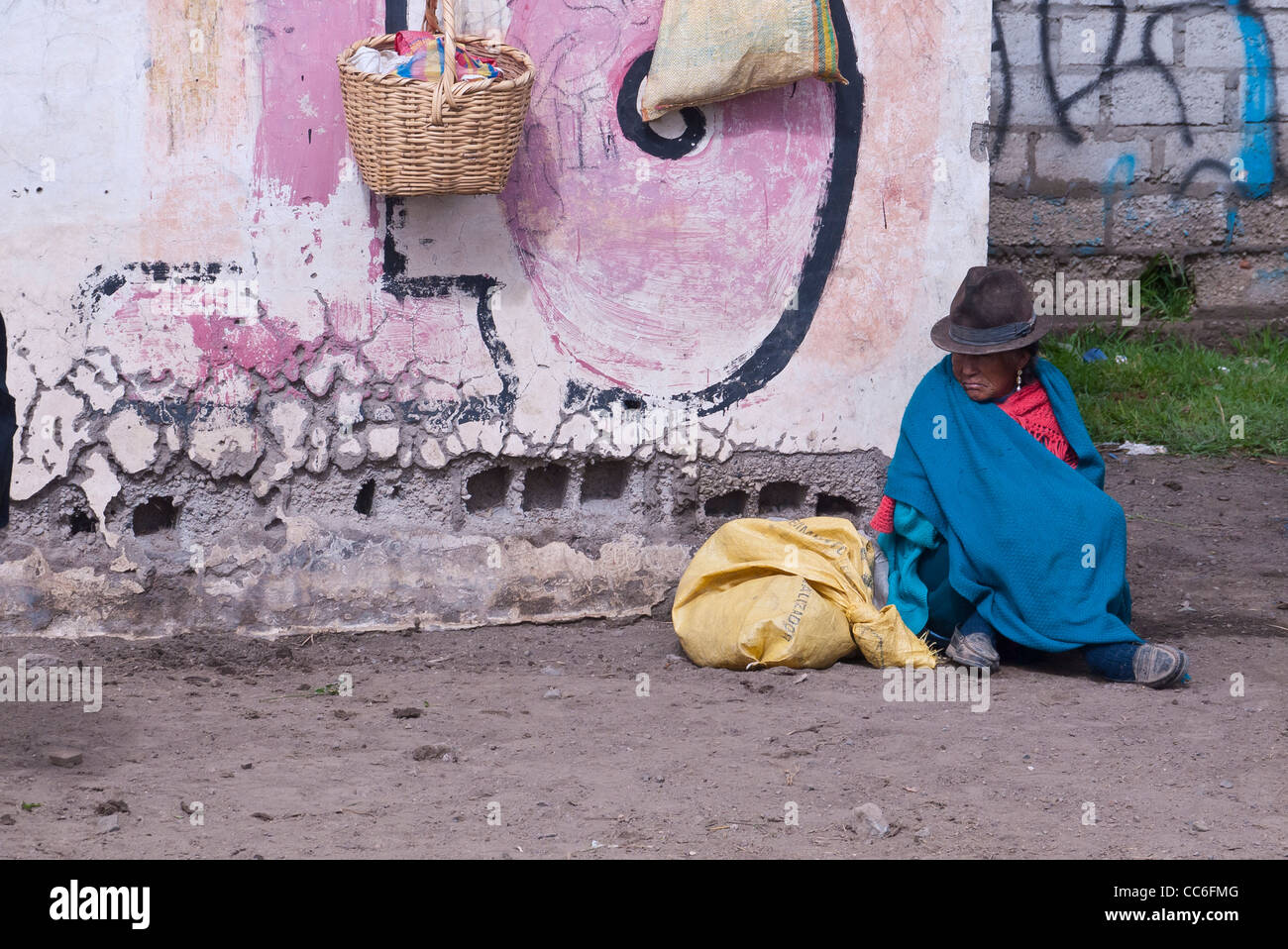 Una vecchia donna indiana andina si siede sul terreno in prossimità di un graffiti parete contrassegnata in Saquisili, Ecuador, Sud America. Foto Stock