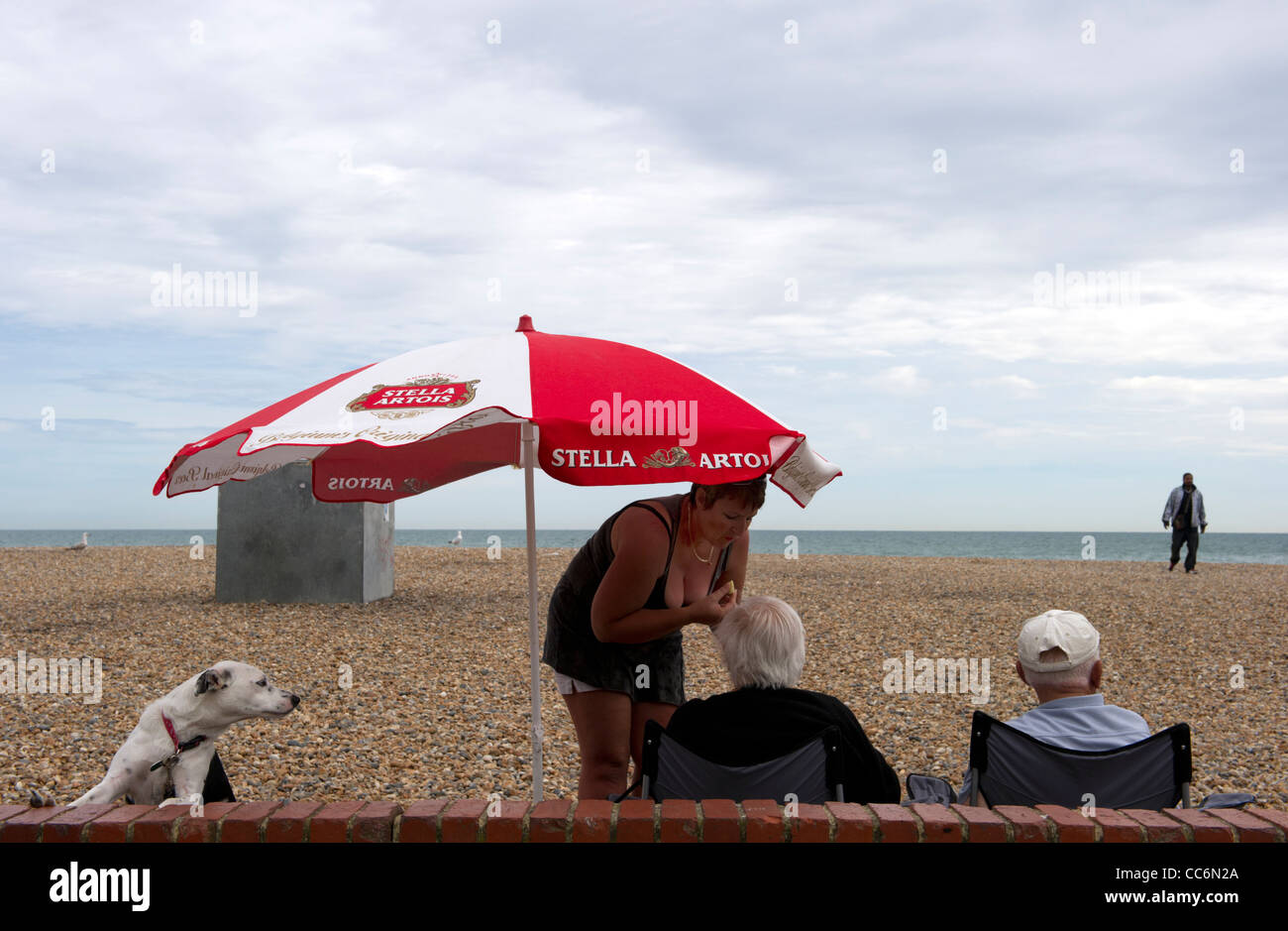Le persone sotto un ombrellone a Brighton con spiaggia ghiaiosa Foto Stock