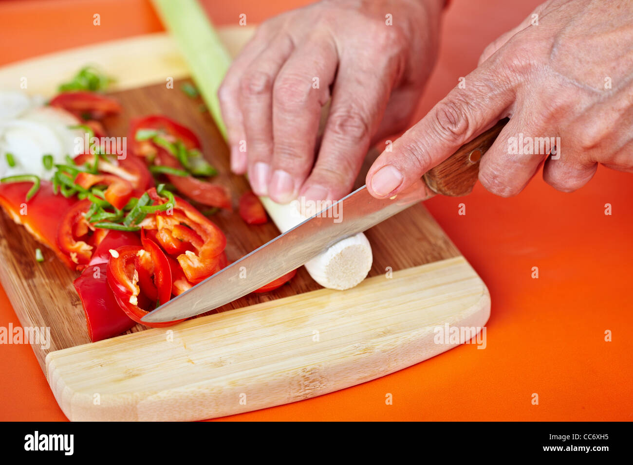 Senior donna mani tritare verdure su una tavola di legno in cucina Foto Stock