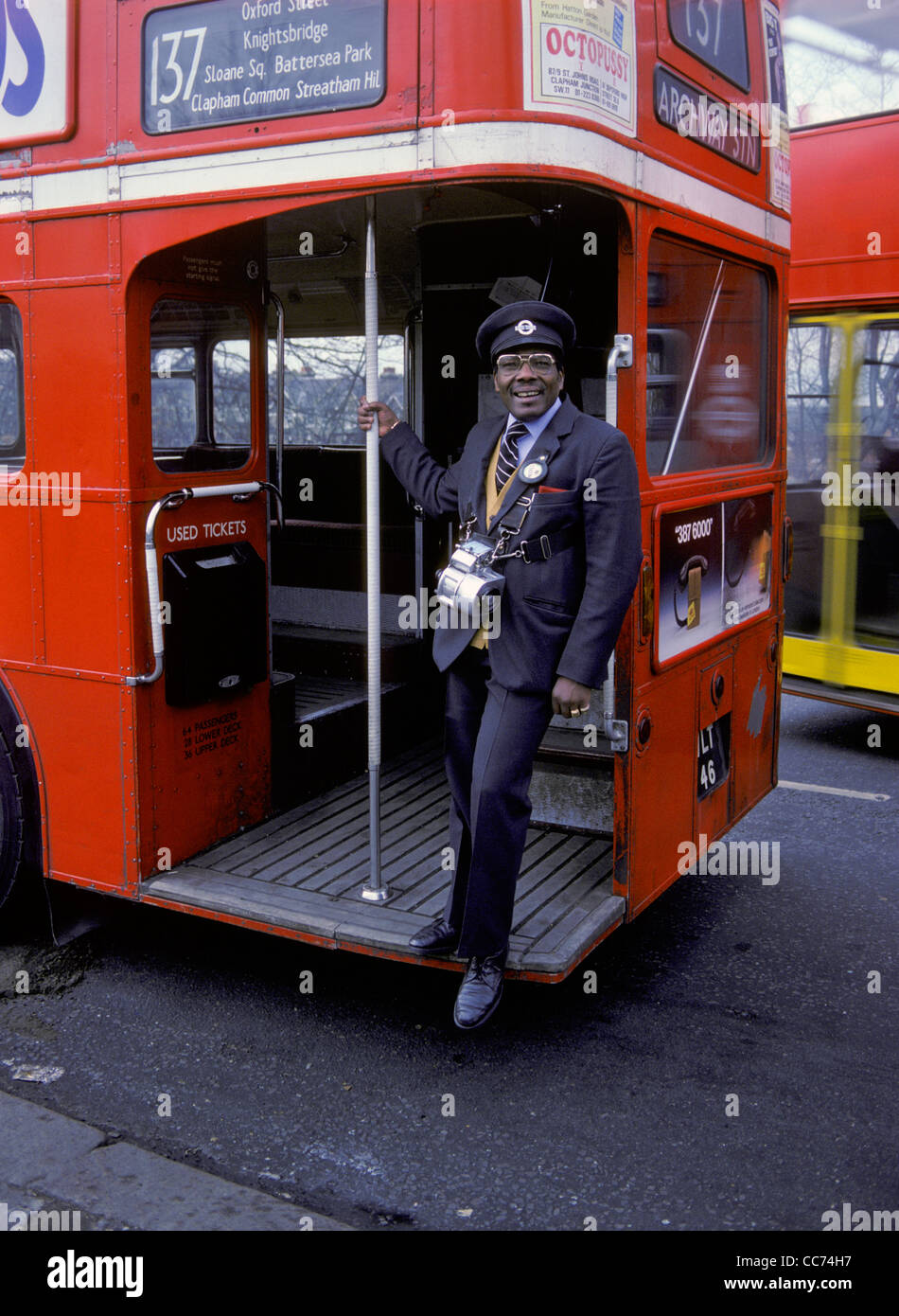 Un West Indian London bus conduttore in piedi sulla piattaforma di una Londra Trasporto autobus Routemaster, grinning al fotografo. Foto Stock