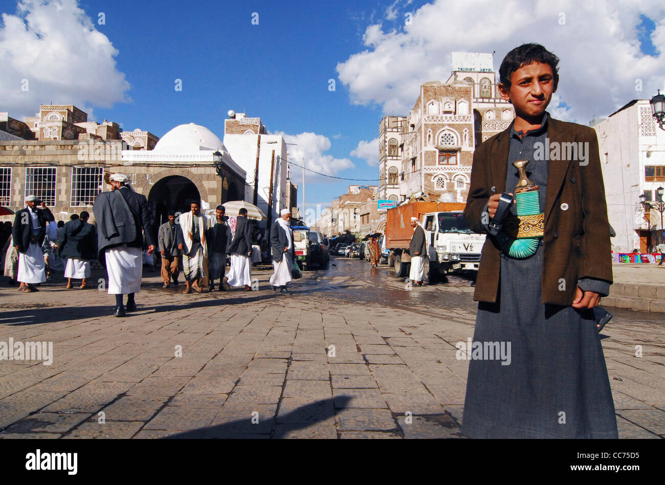 Yemen, Sanaa, basso angolo di visualizzazione tradizionalmente un ragazzo vestito in piedi con la gente che passeggia in background Foto Stock