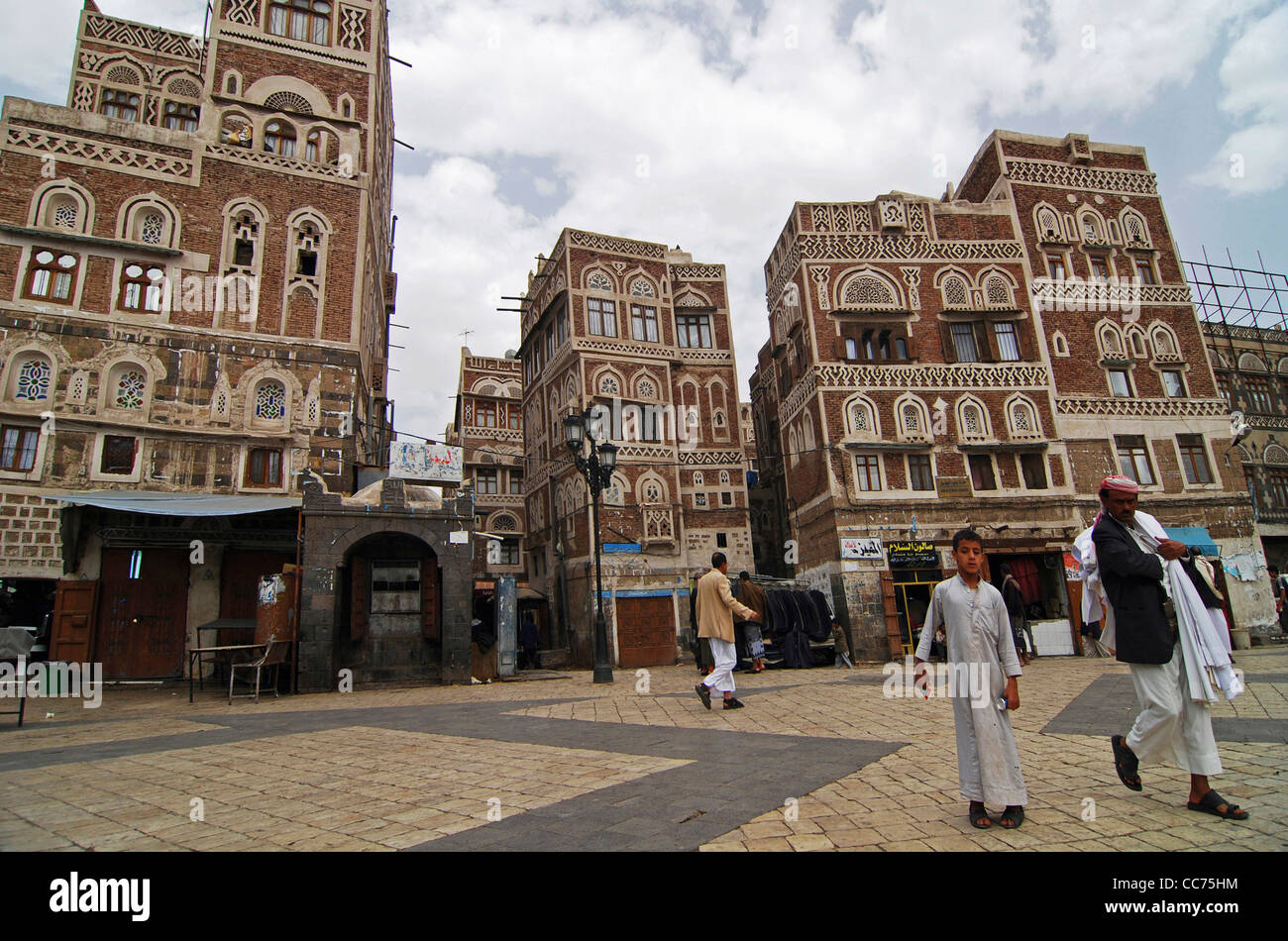 Yemen, Sanaa, gente che cammina sulla strada con edifici in background contro il cielo nuvoloso Foto Stock