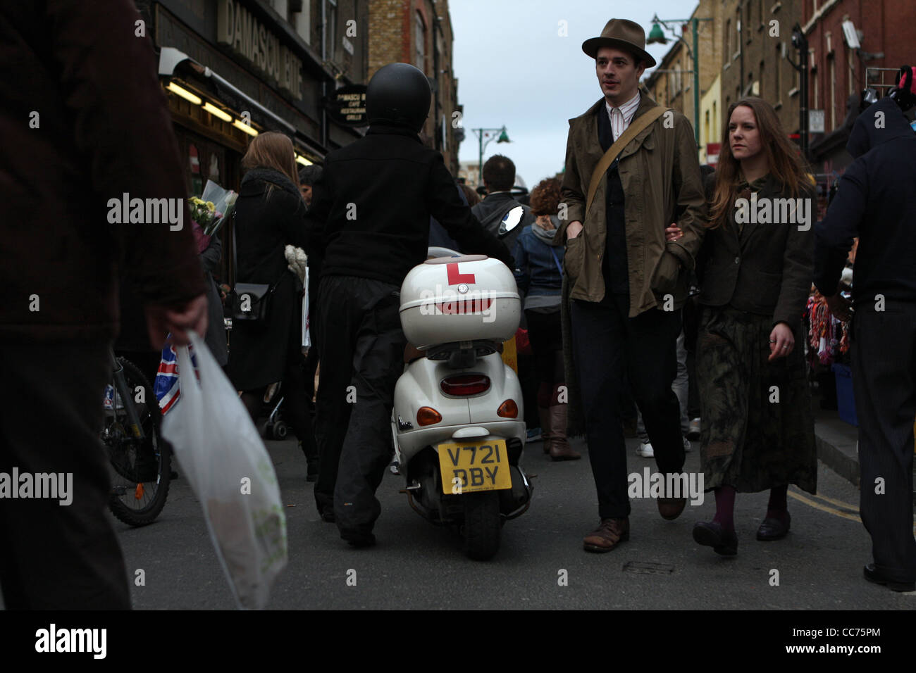 Un uomo che cammina il suo scooter attraverso una strada affollata in east end di Londra Foto Stock