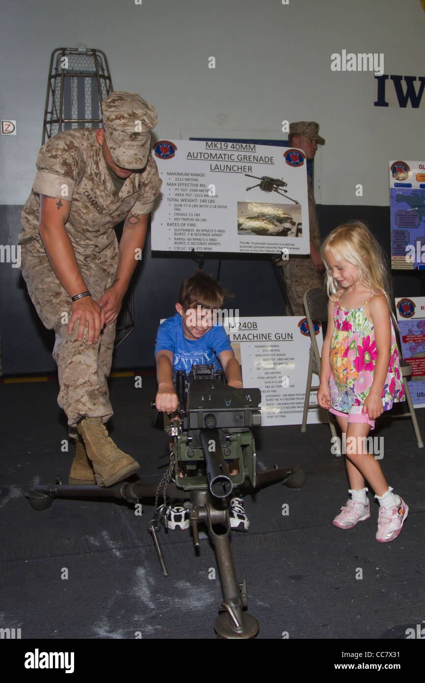 Un giovane ragazzo gioca con una mitragliatrice sulla USS Iwo Jima mentre la sua sorella e un look marino su durante la settimana della flotta 2011 in NYC Foto Stock