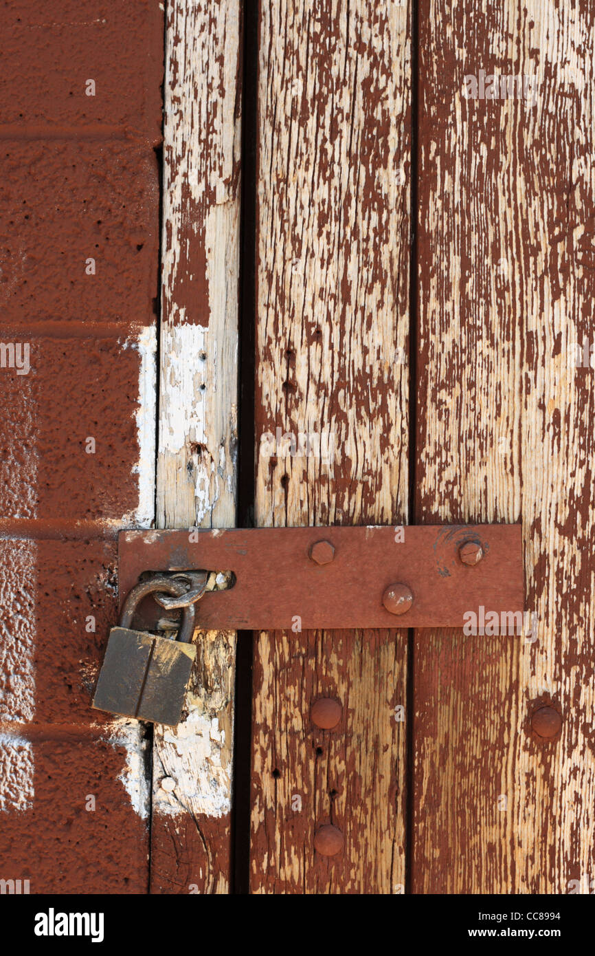 L'immagine verticale della cerniera a occhiello chiuso con lucchetto su un weathered verniciato di marrone porta di legno Foto Stock