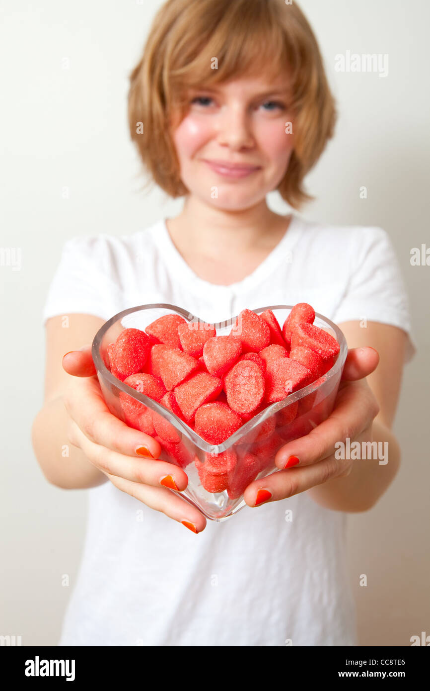 Donna che offre dolci rossi da un cuore ciotola sagomata. Studio shot. Foto Stock
