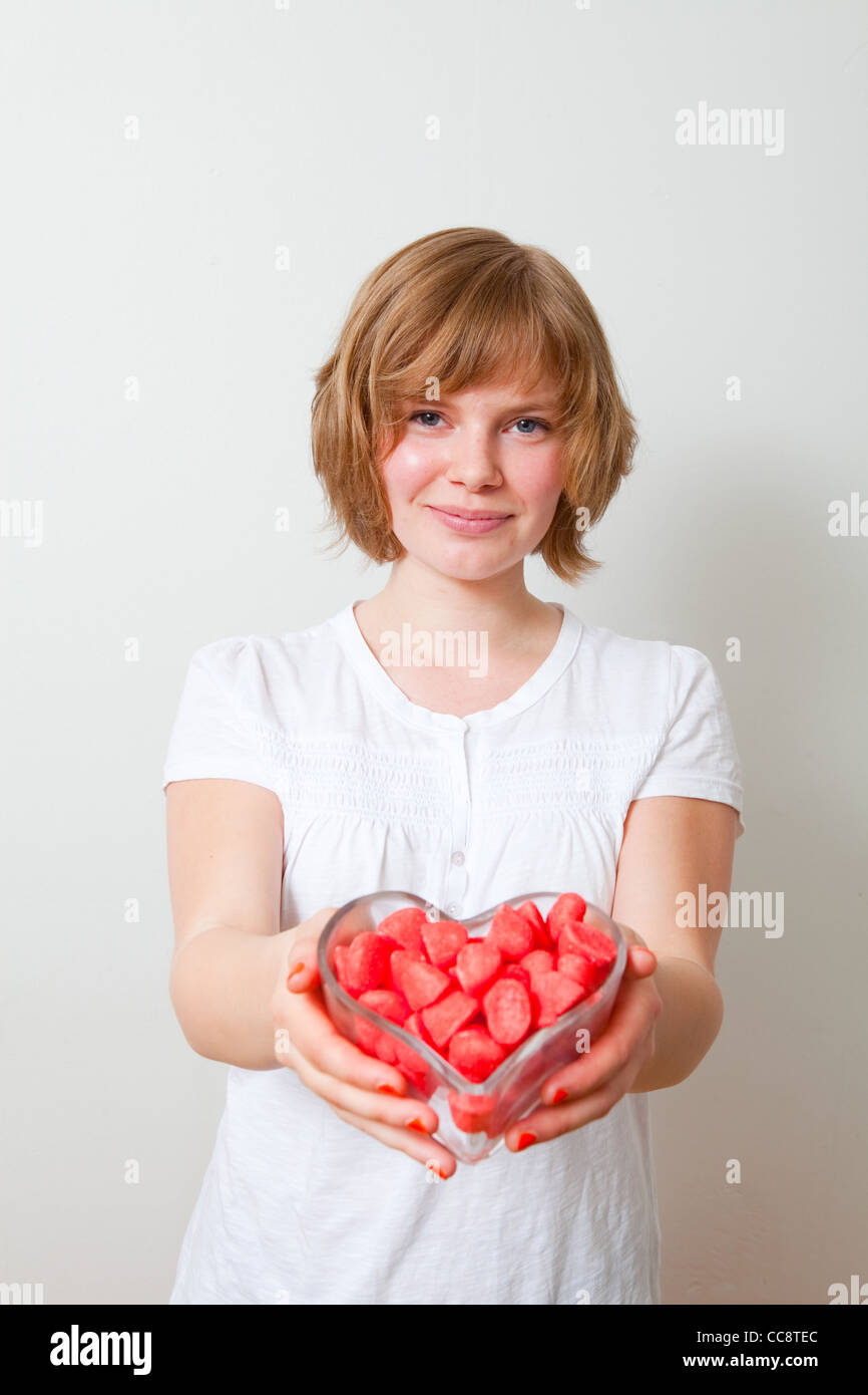 Donna che offre dolci rossi da un cuore ciotola sagomata. Studio shot. Foto Stock